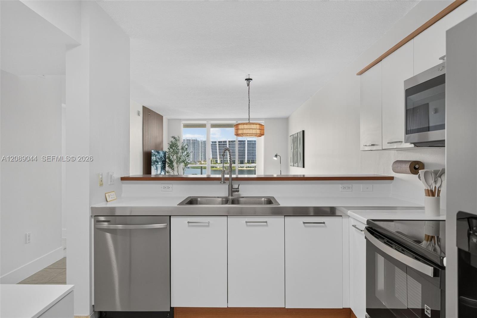 Modern white kitchen with stainless steel appliances and water and high-rise views through the windows.
