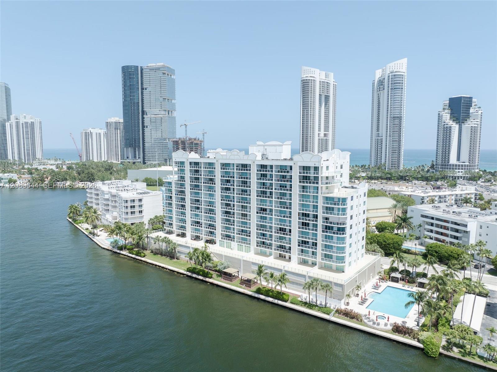 Waterfront condominium with a pool beside the bay, with oceanfront high-rises in the distance.