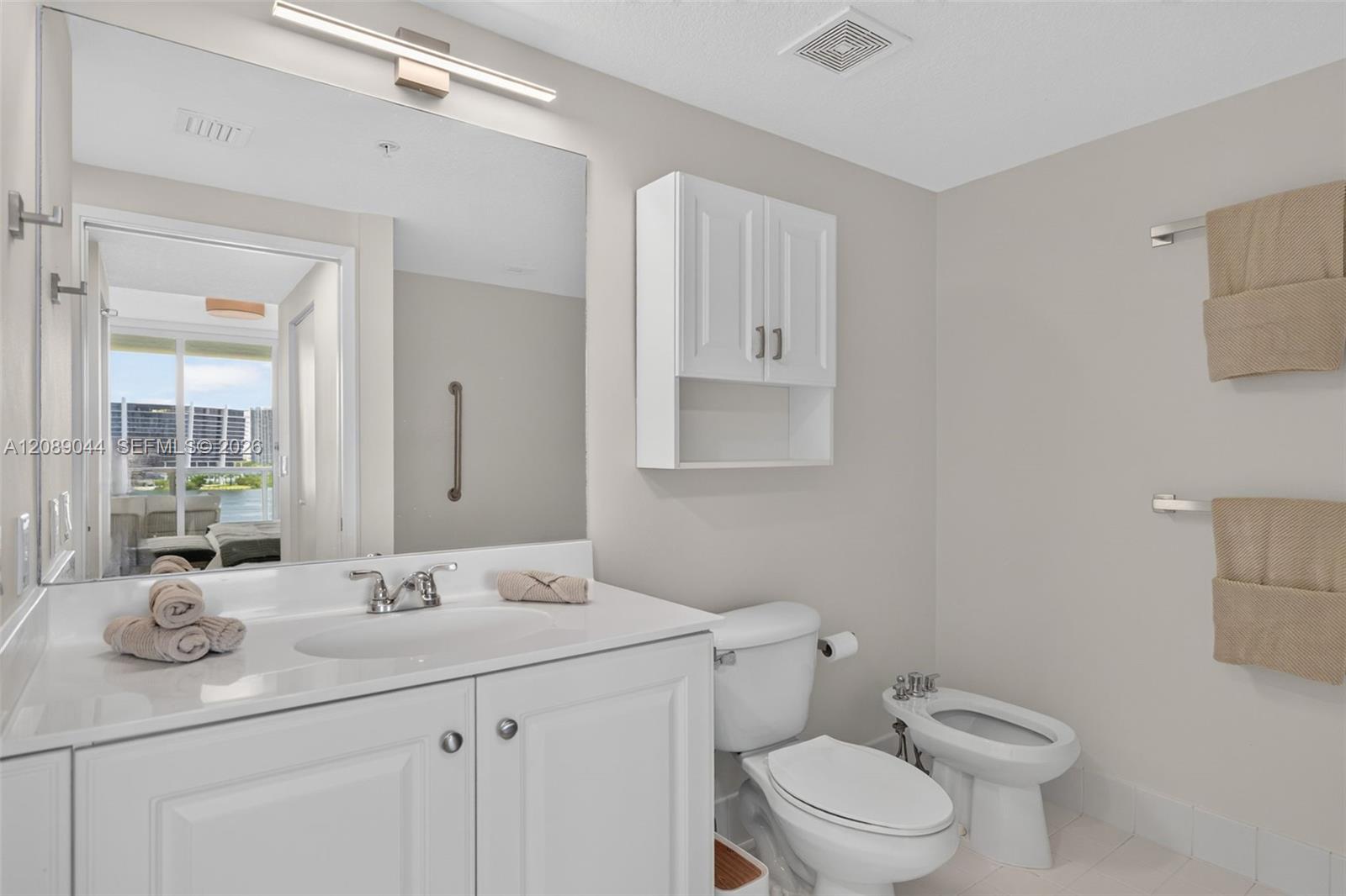 Bathroom with a white vanity and mirror, toilet, bidet, and water visible through the reflected window.