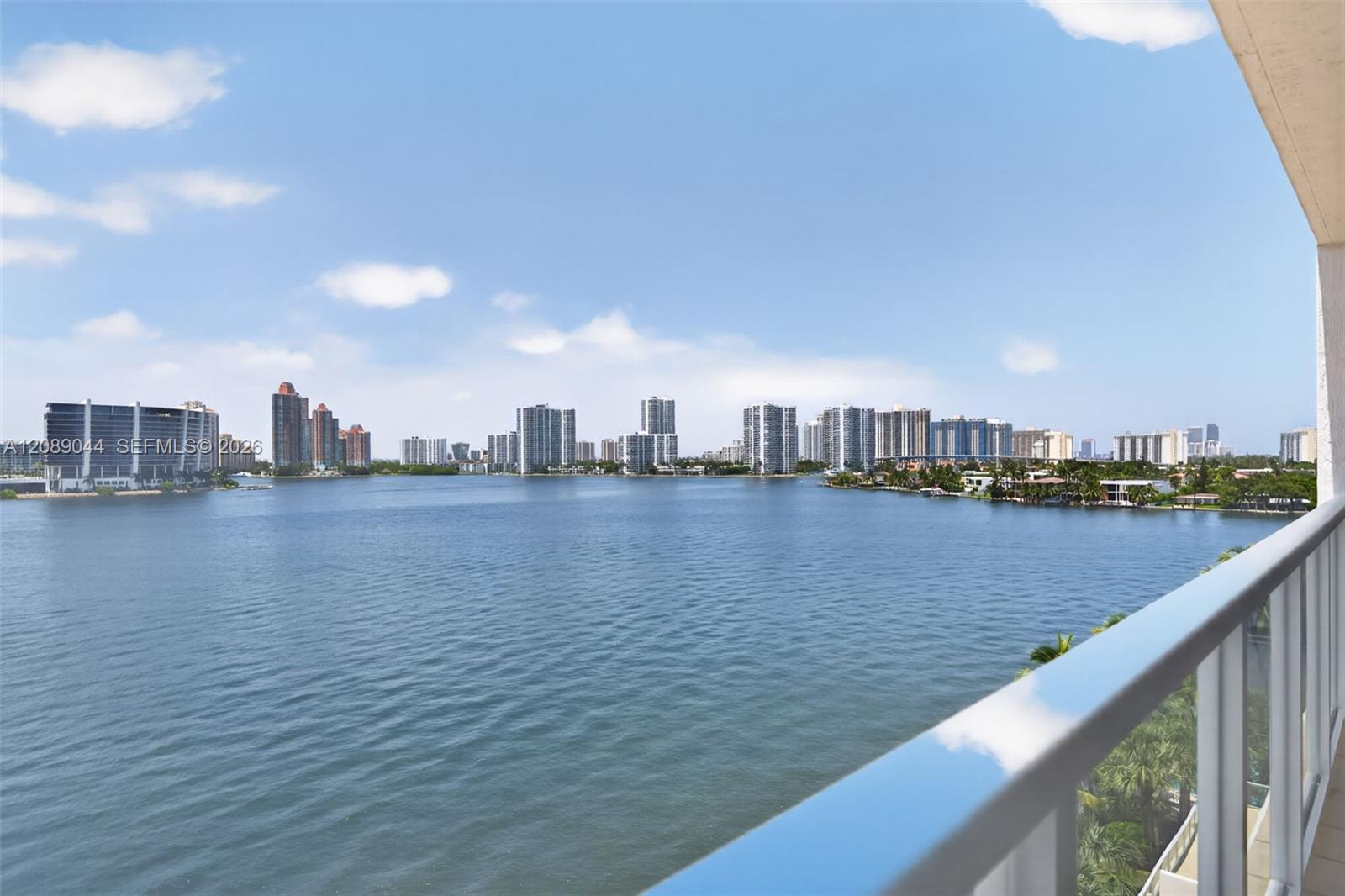 Balcony overlooking a broad bay and waterfront skyline, framed by a glass railing.