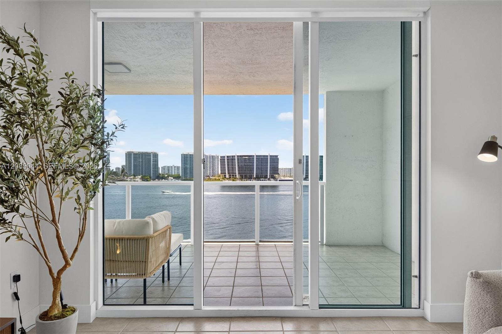 Condo living area opening onto a balcony with water and city views.