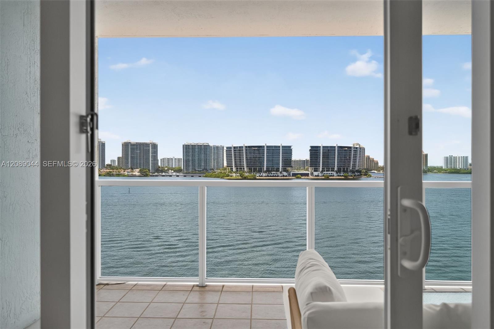 Condo balcony overlooking the bay and waterfront high-rises, seen through open sliding glass doors.