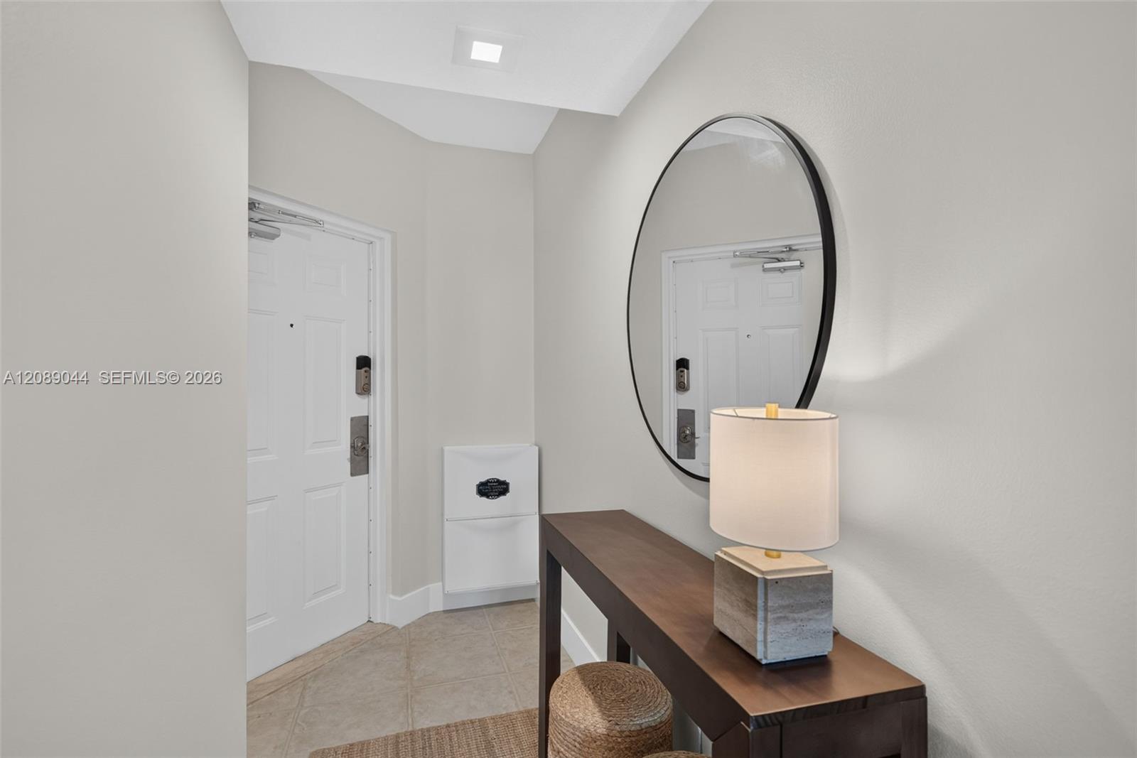 Apartment entry foyer with a tiled floor, oval mirror, and dark console table beside the front door.