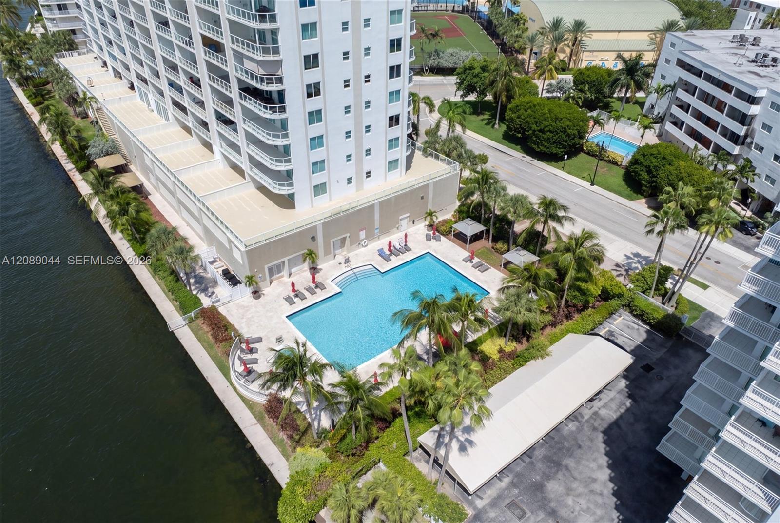 Waterfront condominium with a large swimming pool and palm-lined grounds beside a canal.