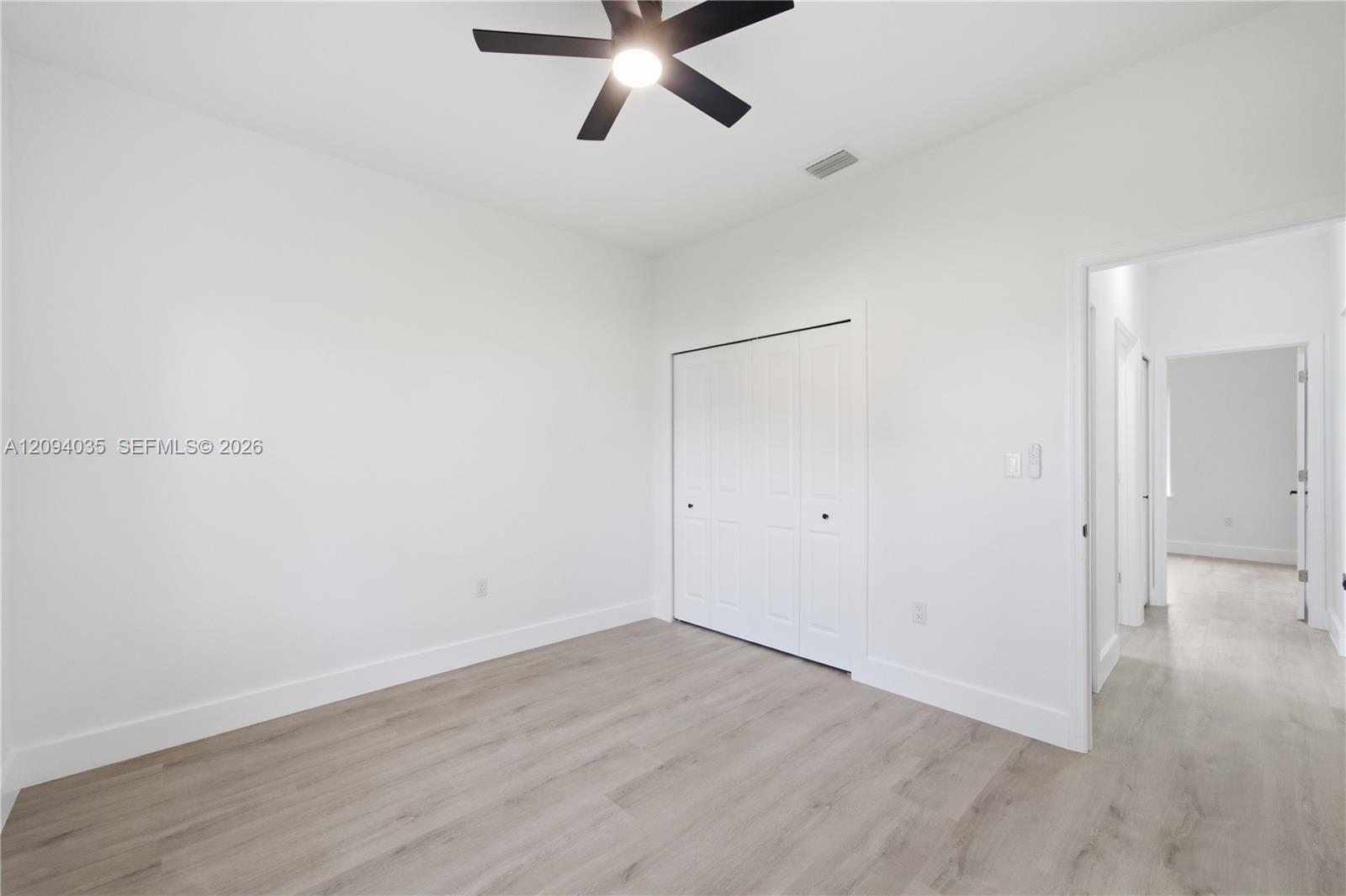 Vacant bedroom with light wood-look flooring, a ceiling fan, and double-door closet.