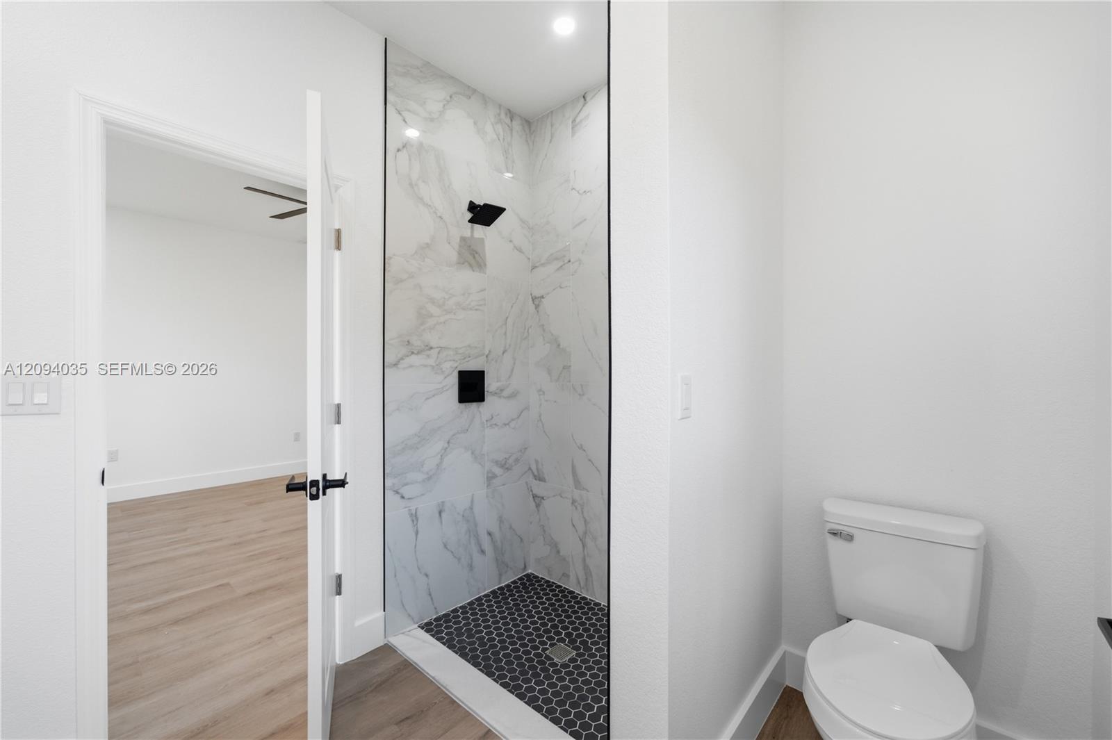 Bathroom with marble-look walk-in shower, black hexagonal floor tile, and white toilet.