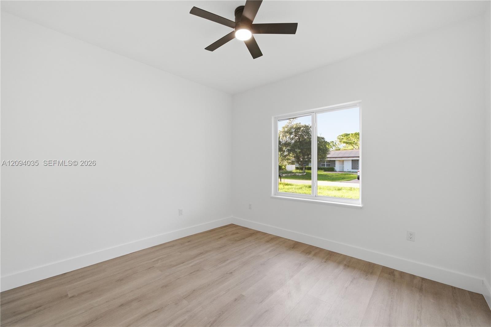 Empty room with light wood-look floors, a ceiling fan, and a large window.