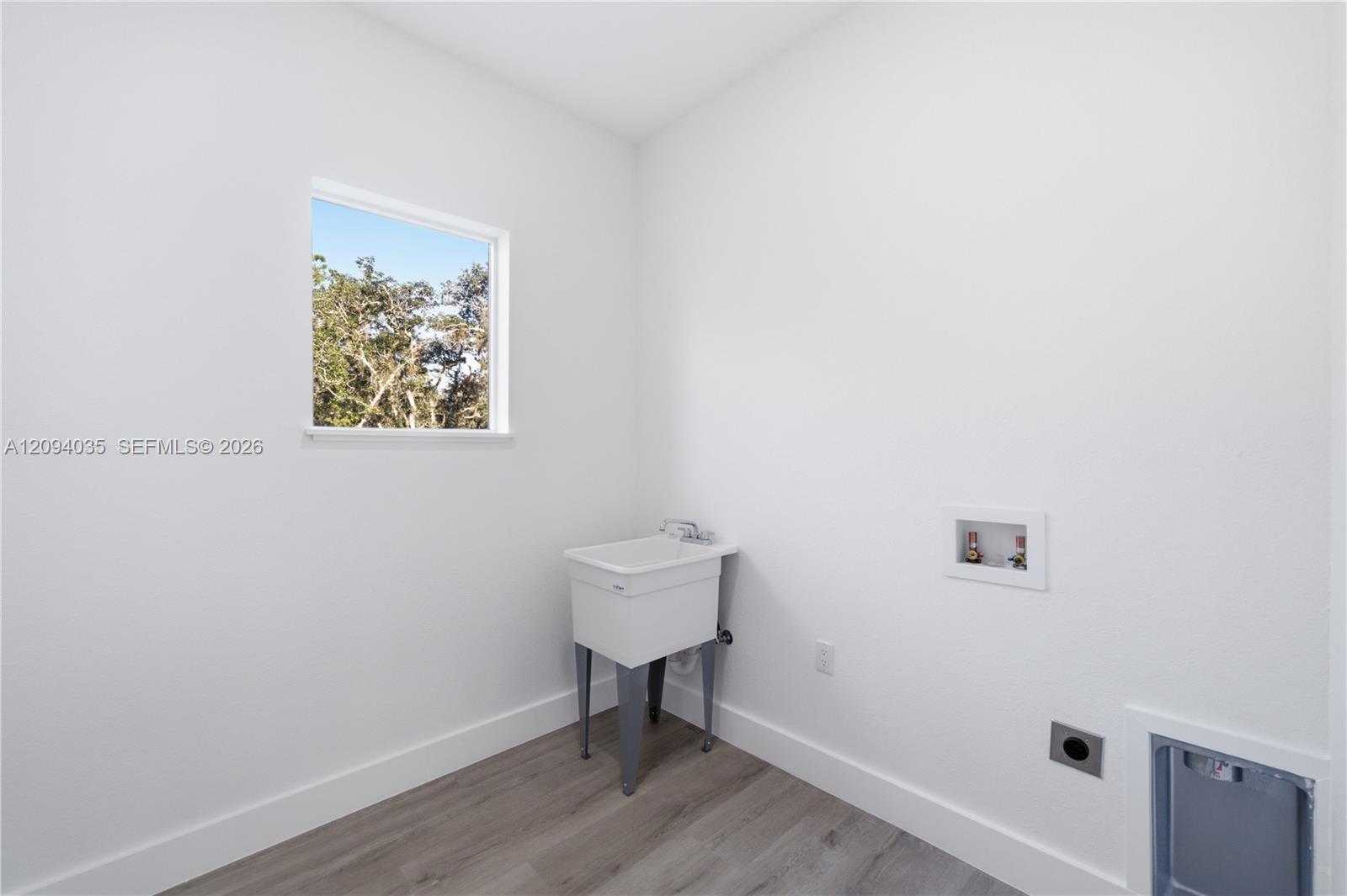 Laundry room with a utility sink, washer hookups, and a window overlooking trees.
