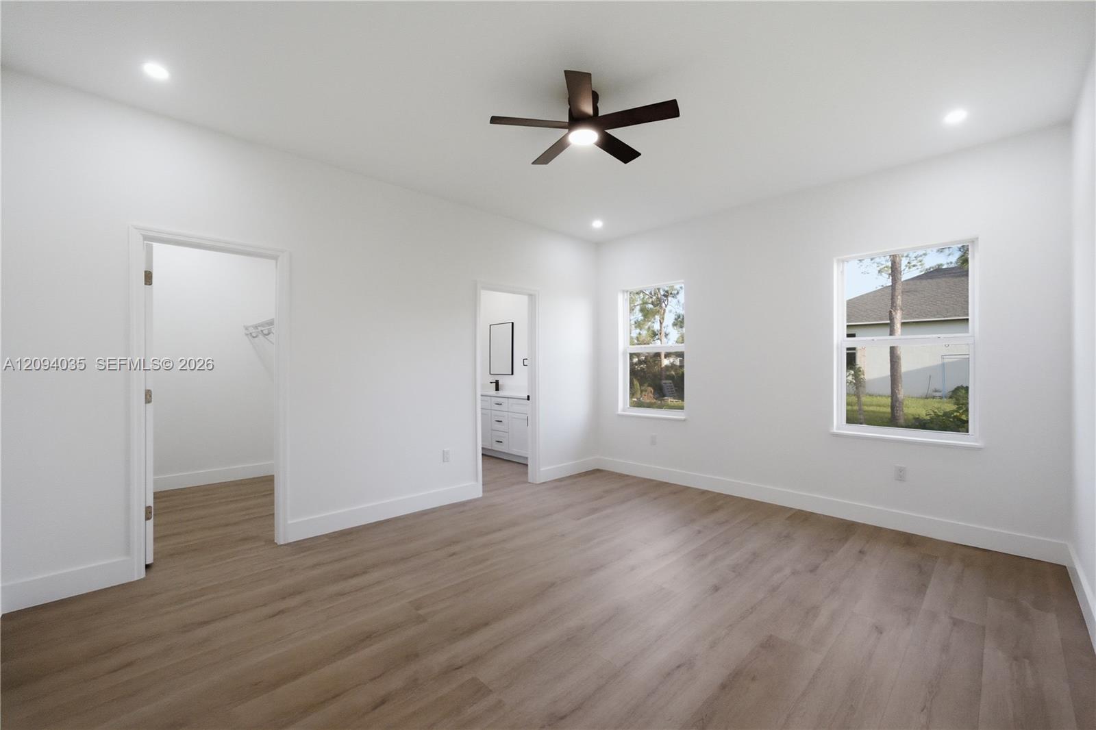 Empty bedroom with wood-look flooring, a dark ceiling fan, and windows overlooking the yard.