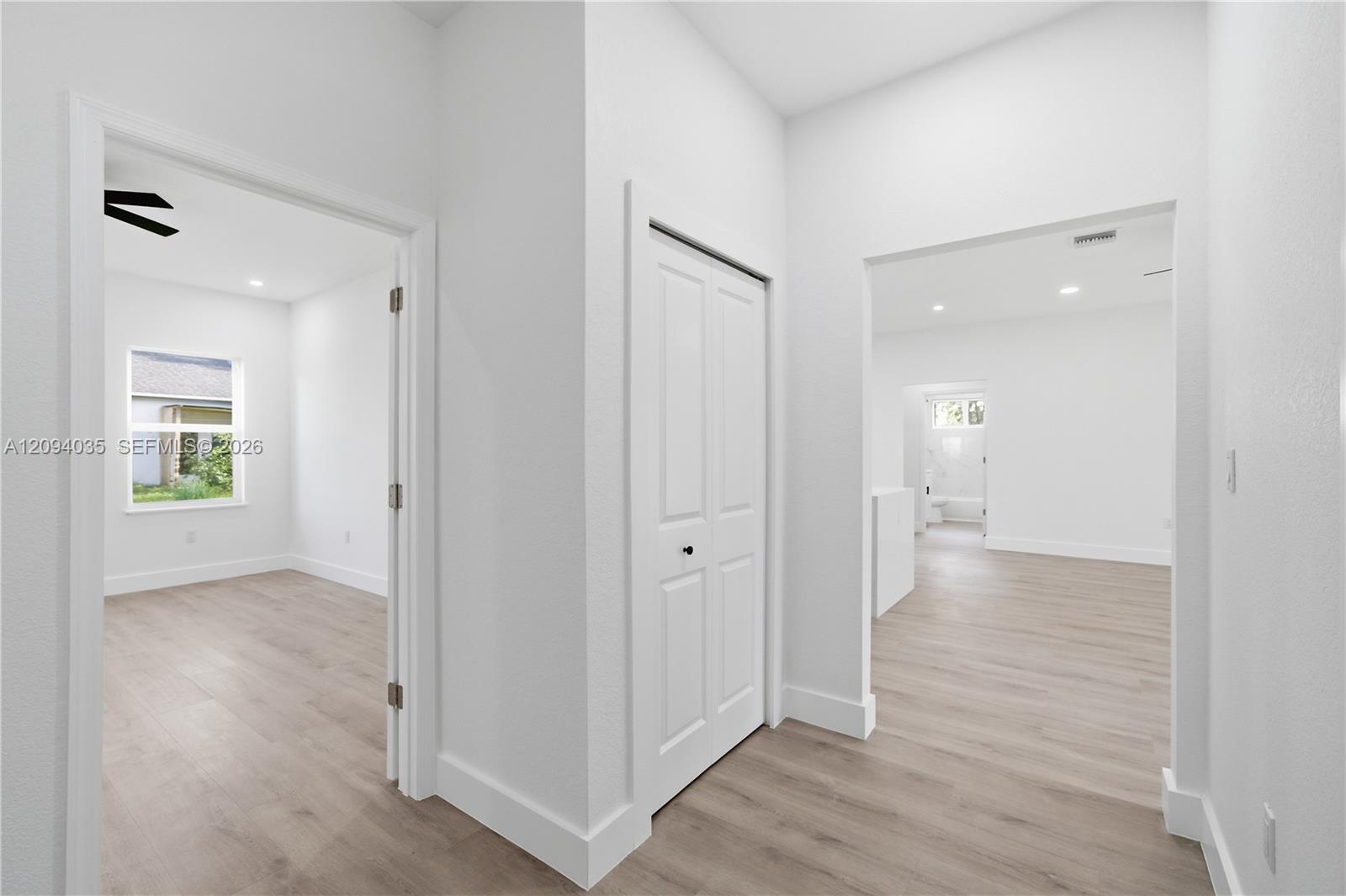 Vacant hallway with light wood-look flooring, a double-door closet, and open adjoining rooms.