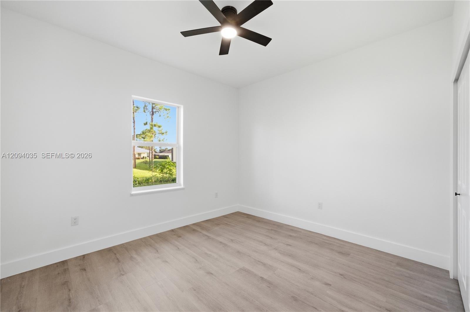 Empty bedroom with light wood-look floors, a ceiling fan, and a window overlooking the yard.