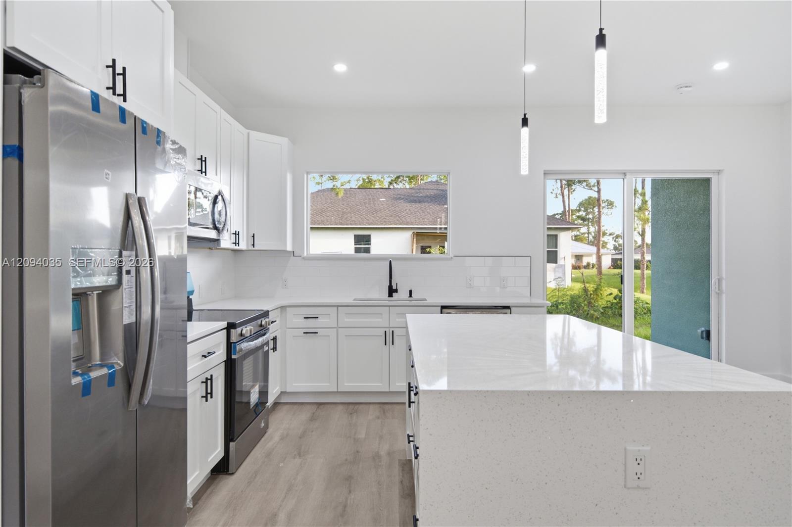 Modern white kitchen with a large island, stainless appliances, and sliding glass doors to the yard.