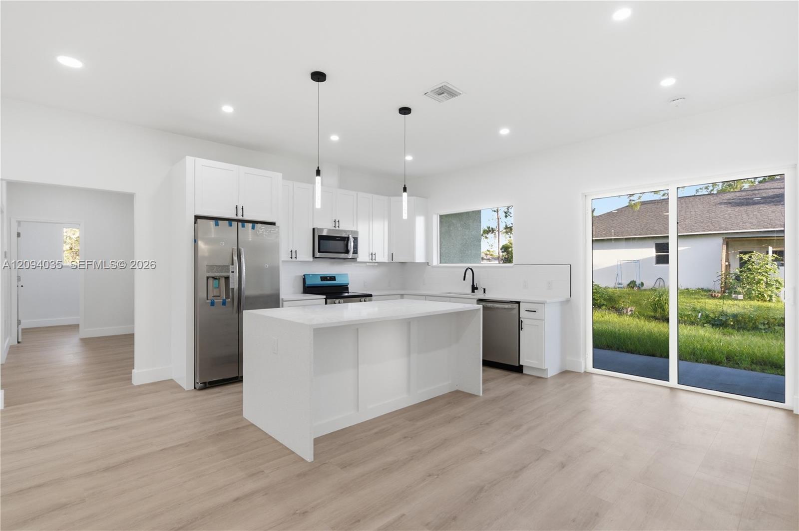 Bright white kitchen with a large island, stainless steel appliances, and sliding glass doors to the yard.