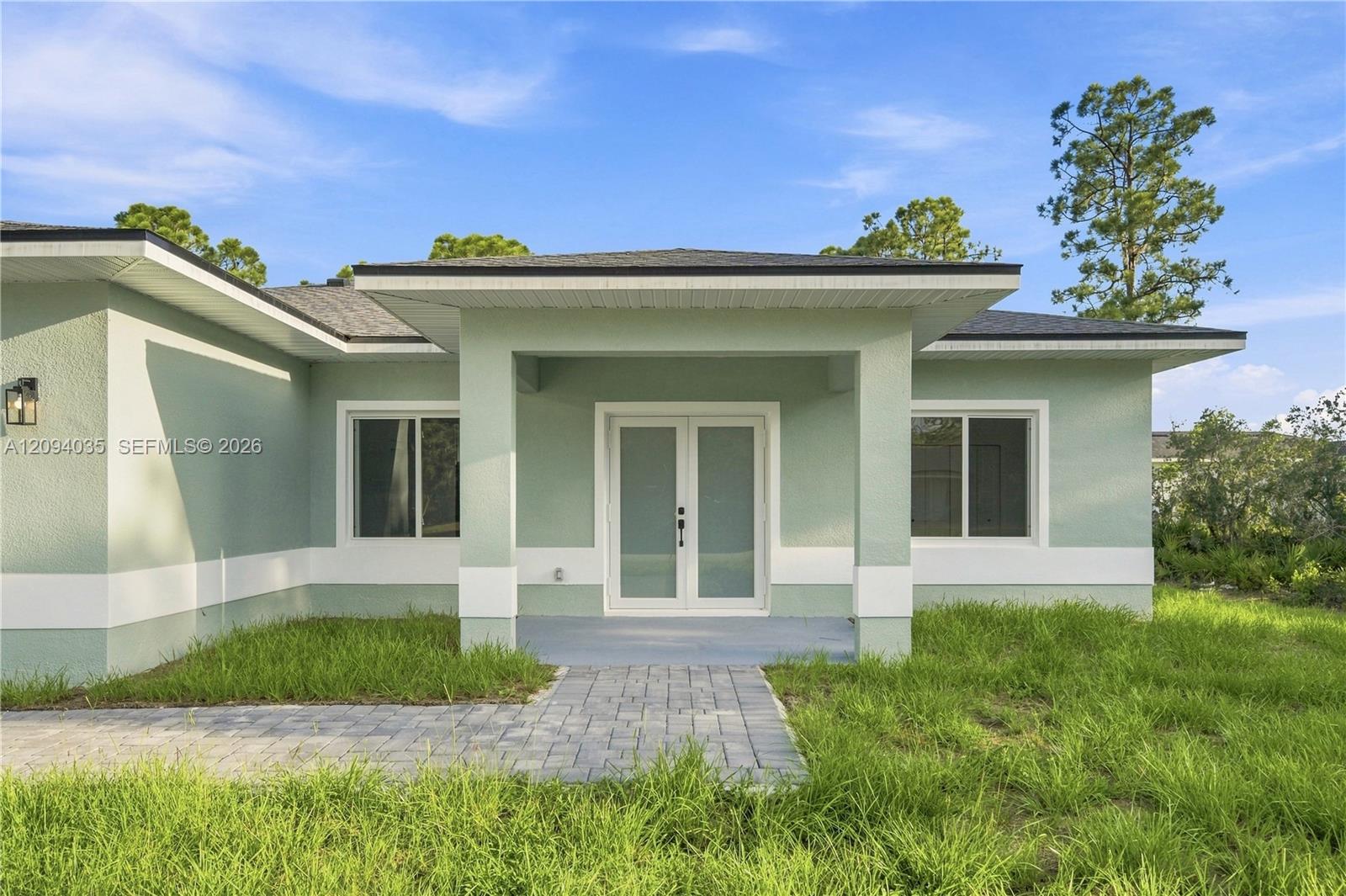 Modern mint-green home with a covered entry and paver walkway across the lawn.