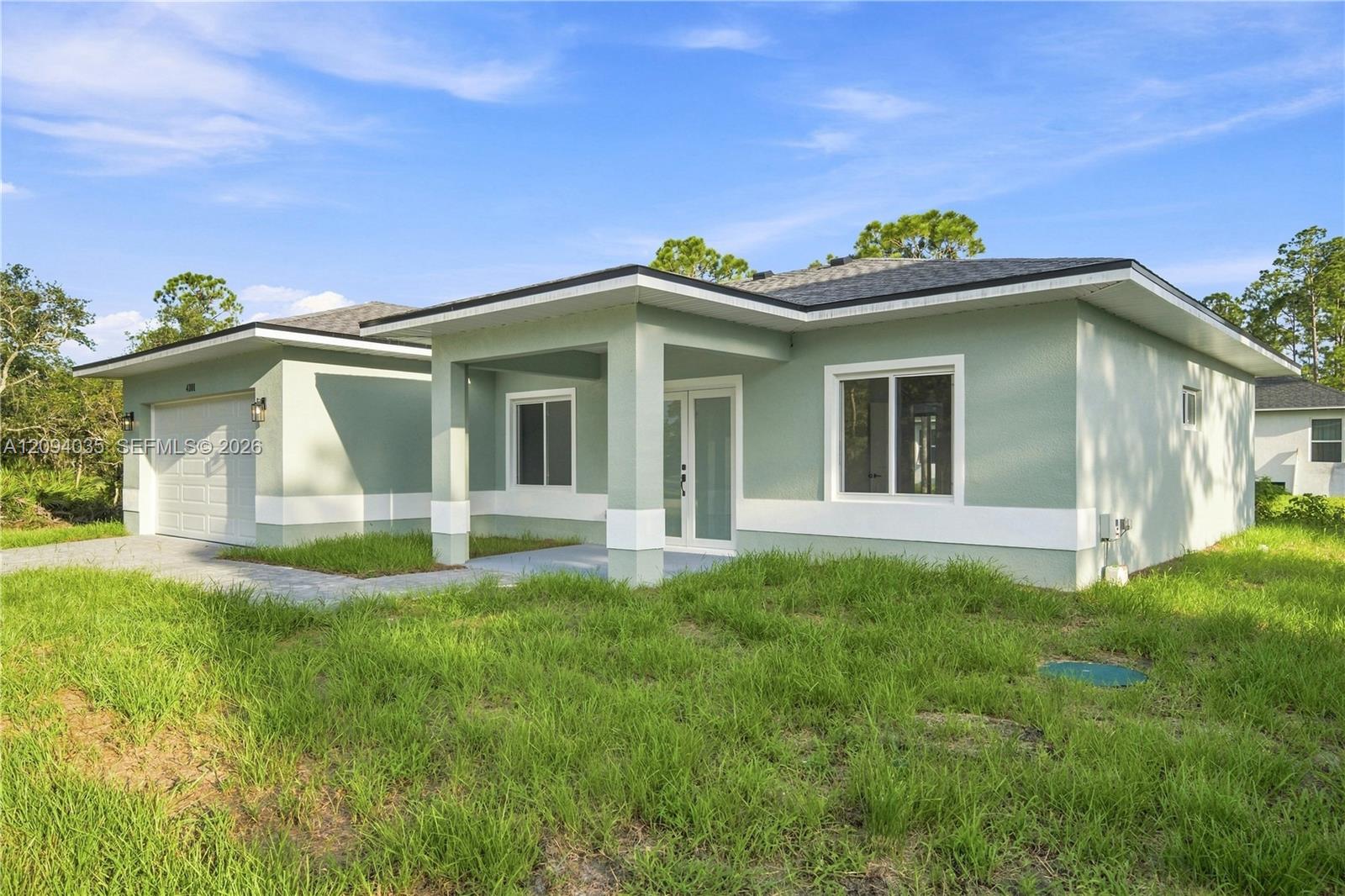 Single-story pale green home with a covered entry, attached garage, and grassy front yard.
