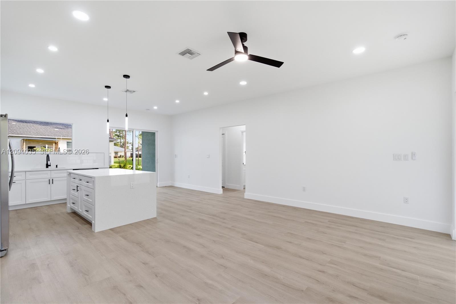 Vacant open-plan living room with white kitchen island, recessed lights, and light wood-look floors.