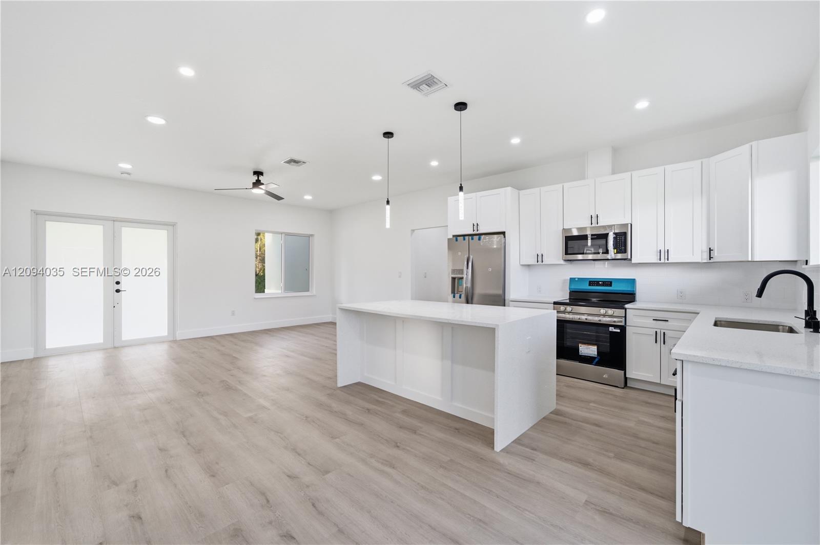 Vacant kitchen with white cabinets, stainless steel appliances, and a large island opening to the living area.