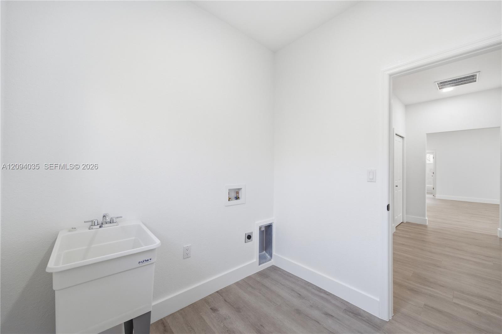 Empty laundry room with a utility sink, washer and dryer hookups, and an open doorway.