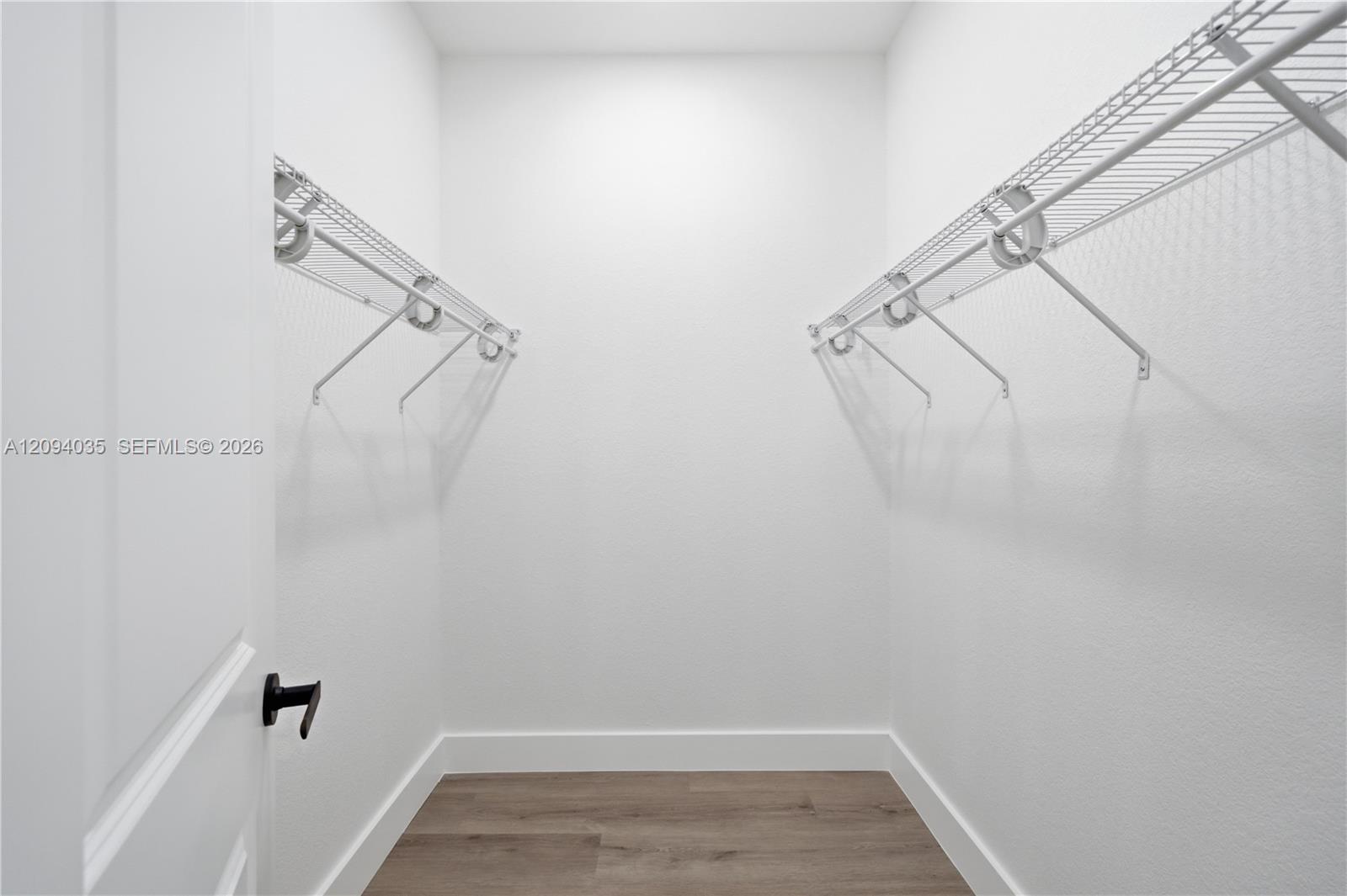 Empty walk-in closet with white walls, wood-look flooring, and wire shelving along both sides.