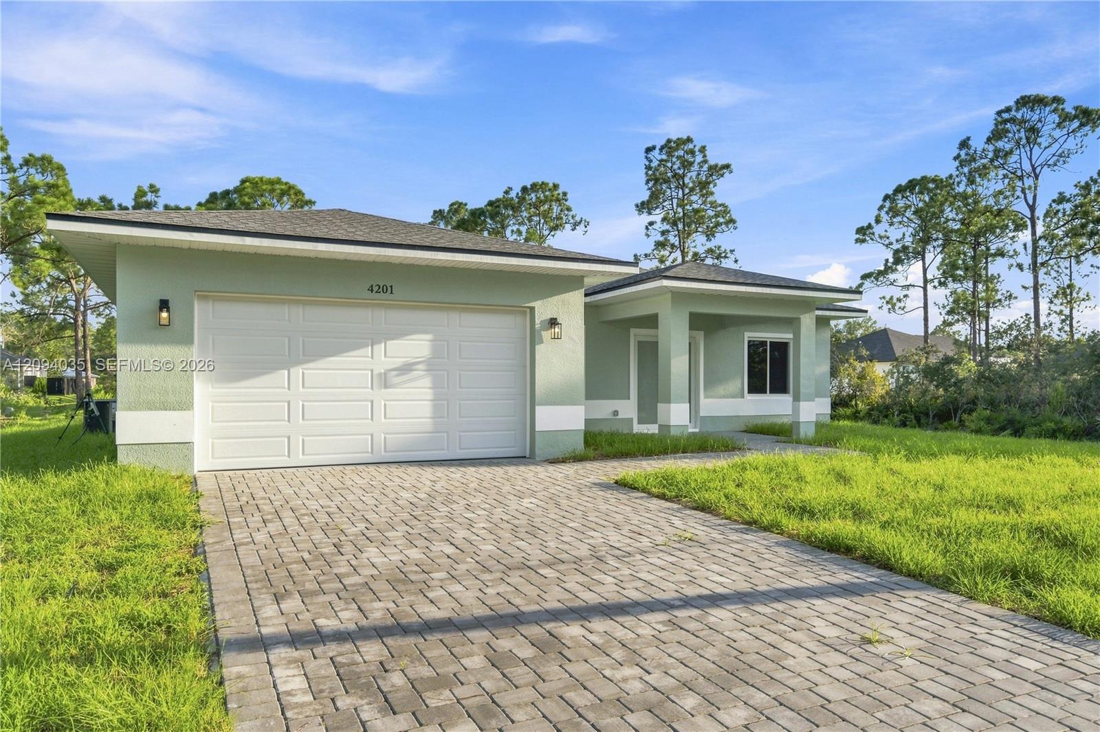 Single-story pale green home with a two-car garage and broad paved driveway.