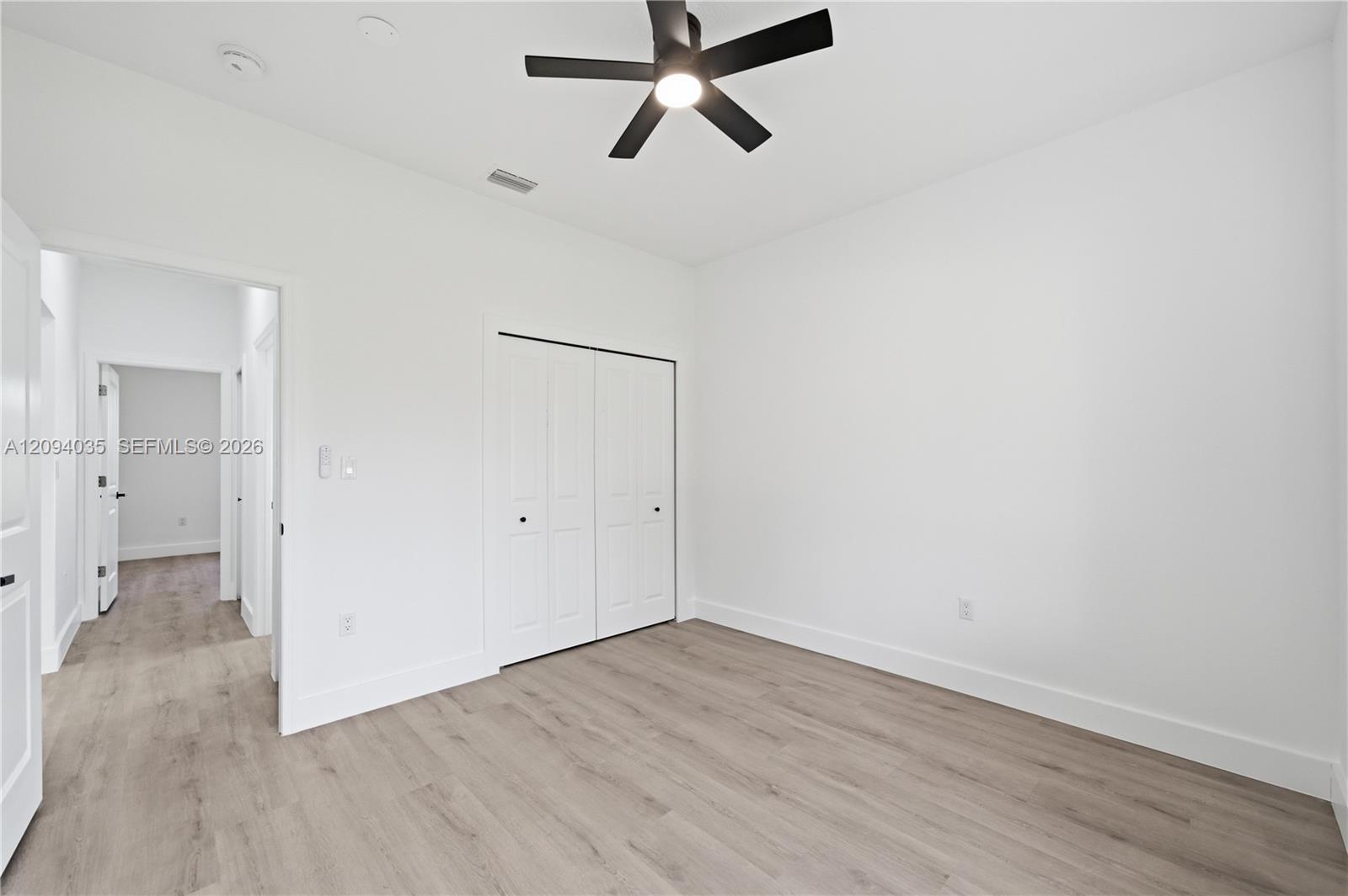 Empty bedroom with light wood-look floors, a black ceiling fan, and a double-door closet.