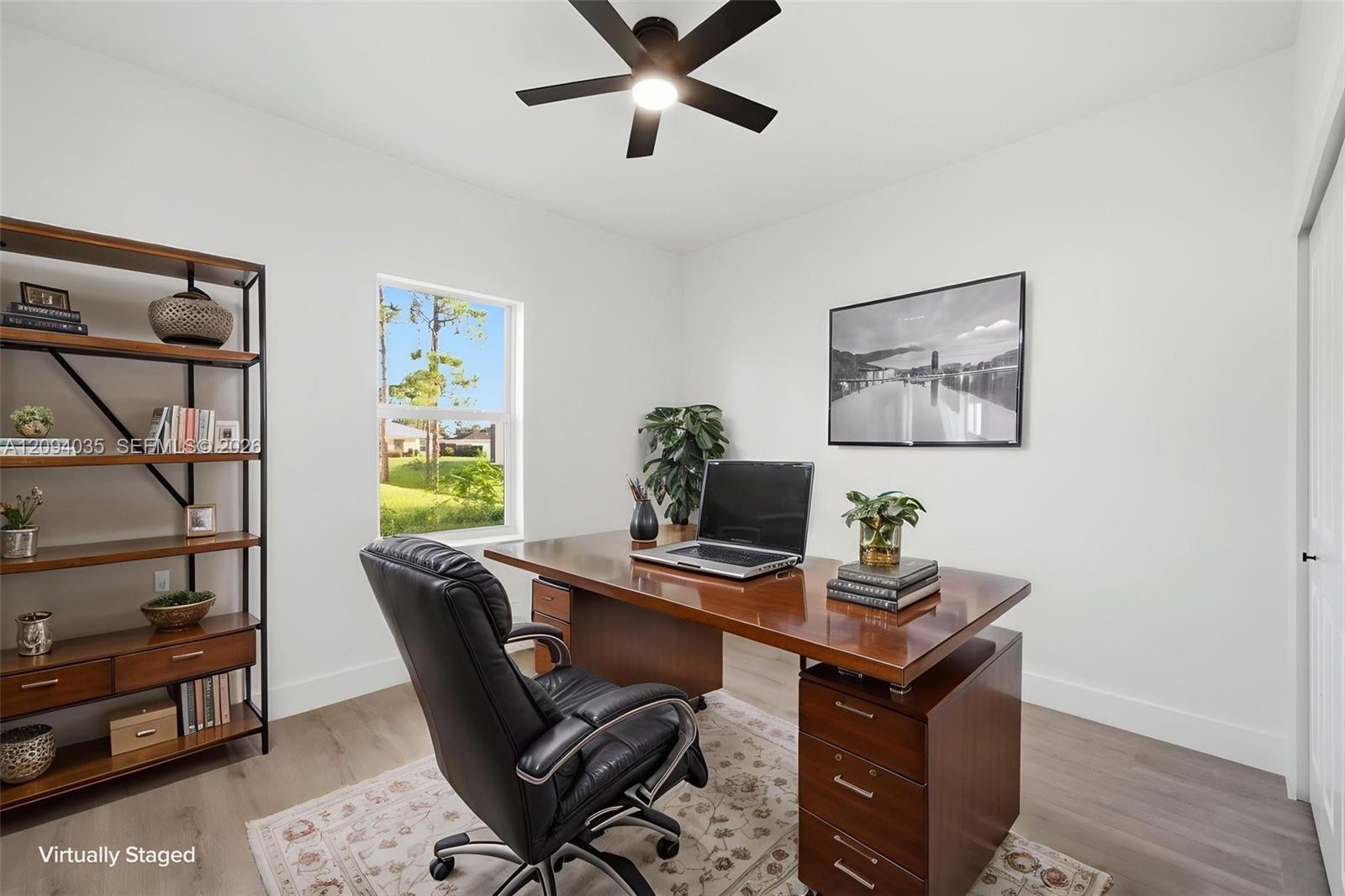 Home office with a wooden desk, black chair, open laptop, and window overlooking a green yard.
