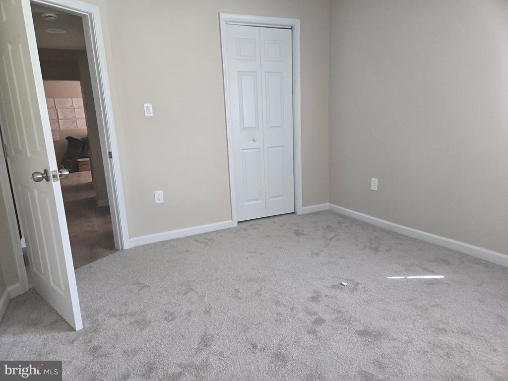Empty bedroom with gray carpet, white closet doors, and an open doorway.