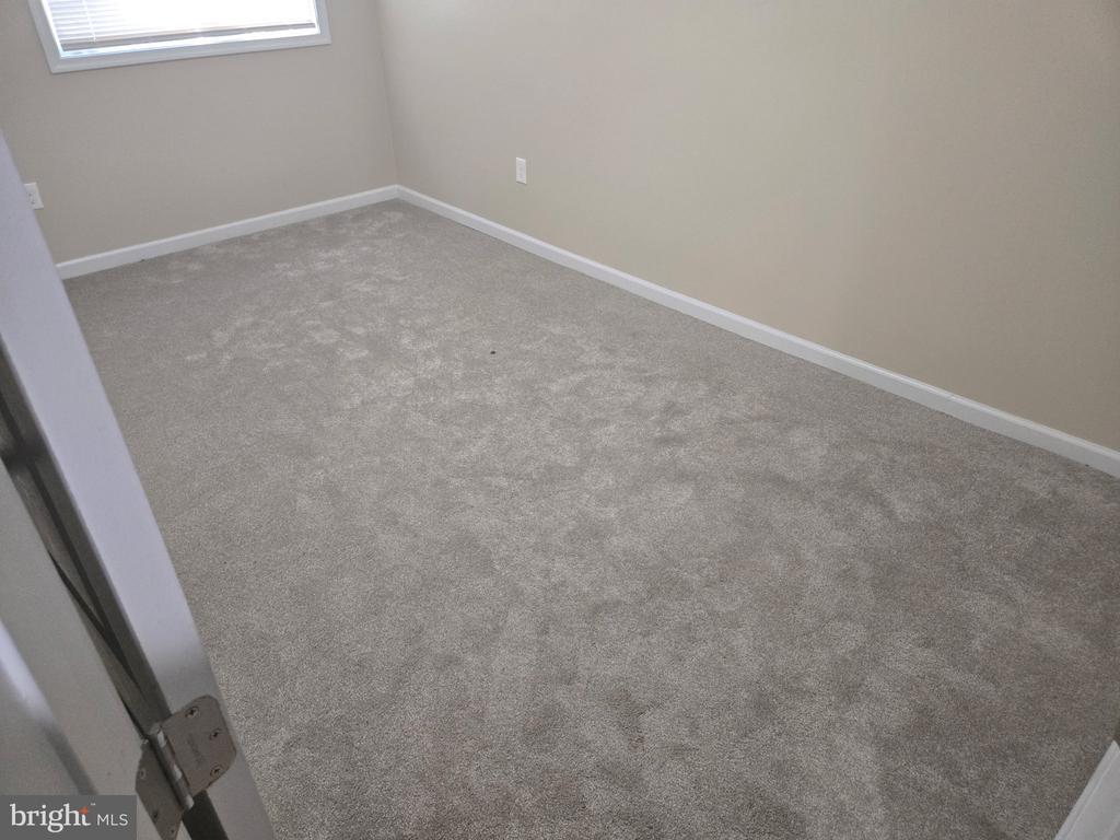 Empty carpeted bedroom with beige walls and a window with blinds.