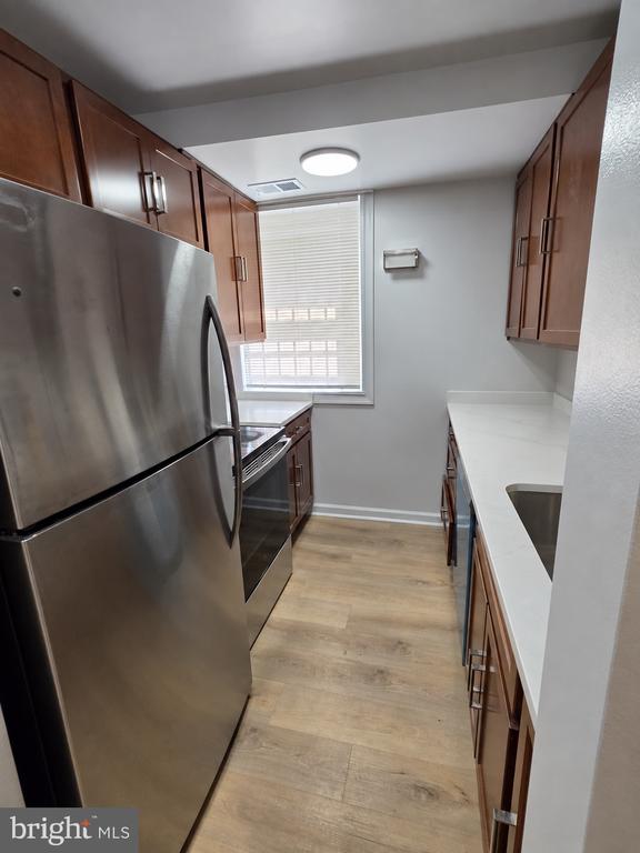 Galley kitchen with stainless steel appliances, white countertops, and dark wood cabinetry.