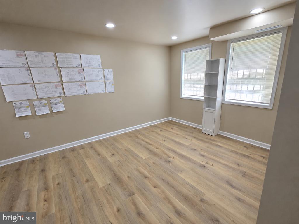 Empty room with wood-look flooring, two windows, and plans displayed on the wall.