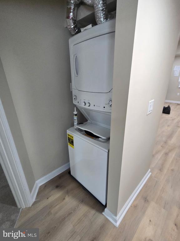Stacked washer and dryer in a narrow laundry alcove with light wood-look flooring.