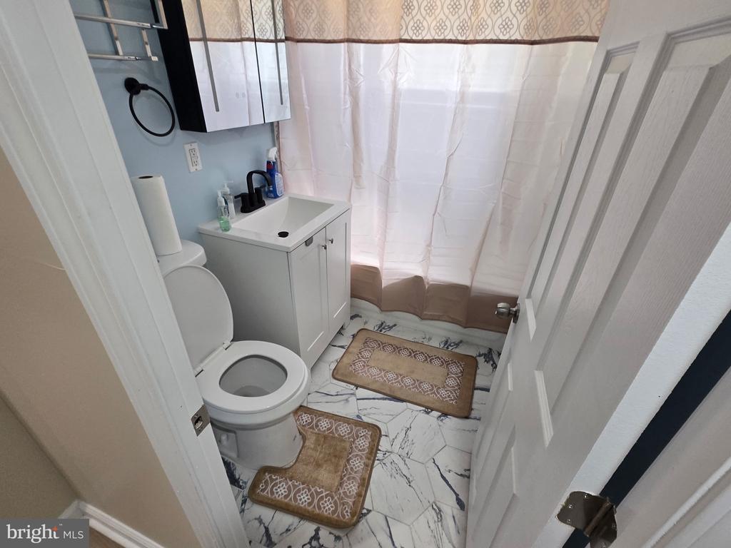 Bathroom with a white vanity and toilet, patterned shower curtain, and marble-look tile floor.