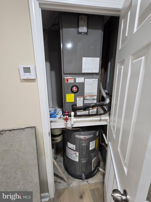 Utility closet with a heating and cooling unit above a large water heater and exposed plumbing.