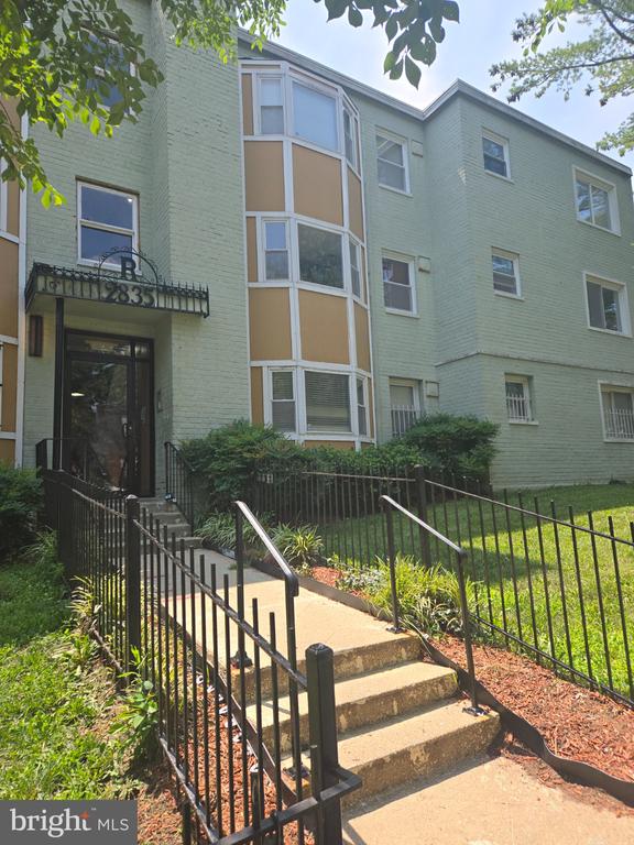 Pale green brick apartment building with bay windows and a railed entrance stairway.