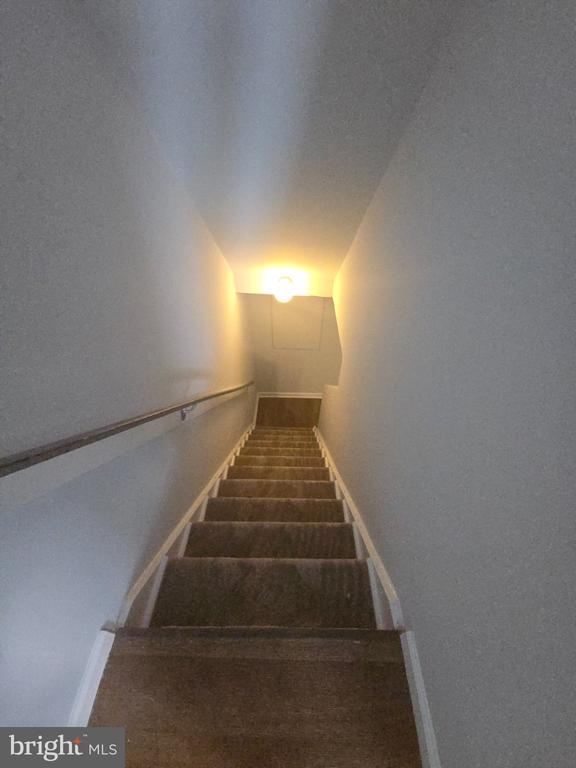 Carpeted staircase with a wooden handrail and a light at the top.