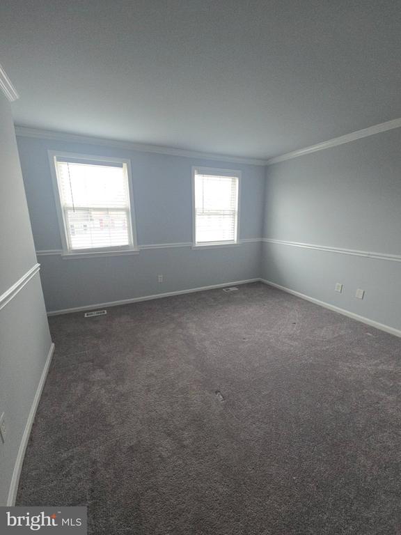 Empty carpeted room with two windows, blinds, and chair rail molding.