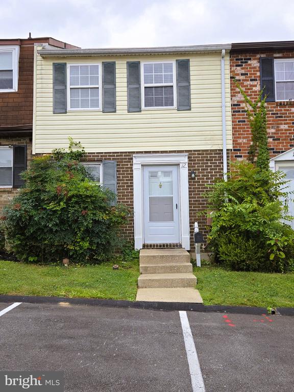 Attached home with pale yellow siding, brick lower level, white entry door, and front steps.