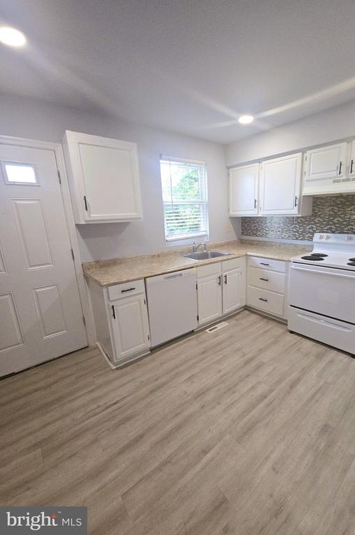 Kitchen with white cabinets, gray tile backsplash, and light wood-look flooring.