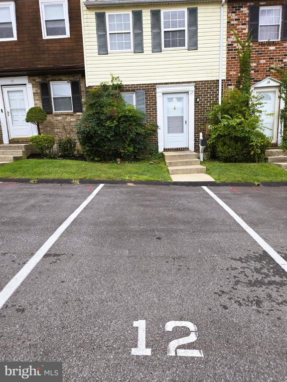 Townhouse front with a white entry door, brick lower level, shrubs, and parking space marked 12.