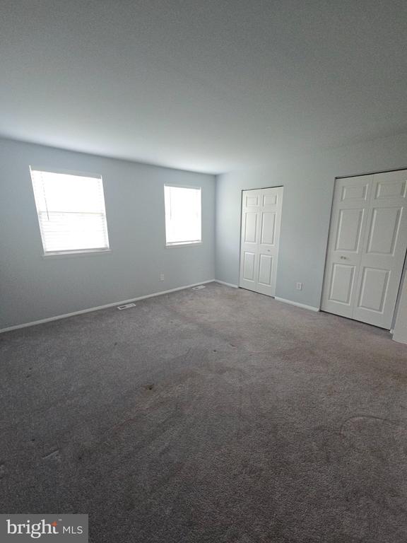Vacant carpeted bedroom with two windows and two white paneled doors.