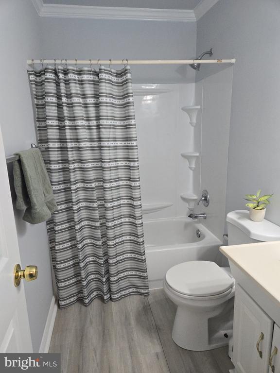 Bathroom with a striped shower curtain, white tub, toilet, and gray wood-look flooring.