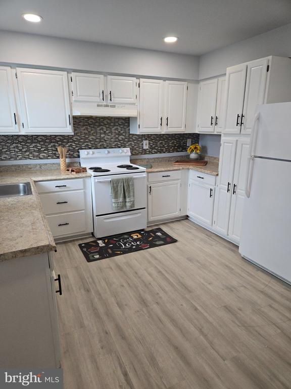 Kitchen with white cabinets, electric range, patterned backsplash, and light wood-look flooring.