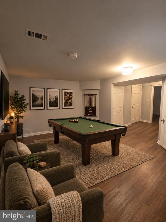 Furnished recreation room with a green-felt pool table, sofas, and framed artwork.