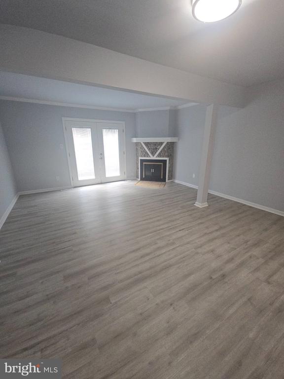 Empty living room with light wood-look flooring, a decorative fireplace, and double glass doors.