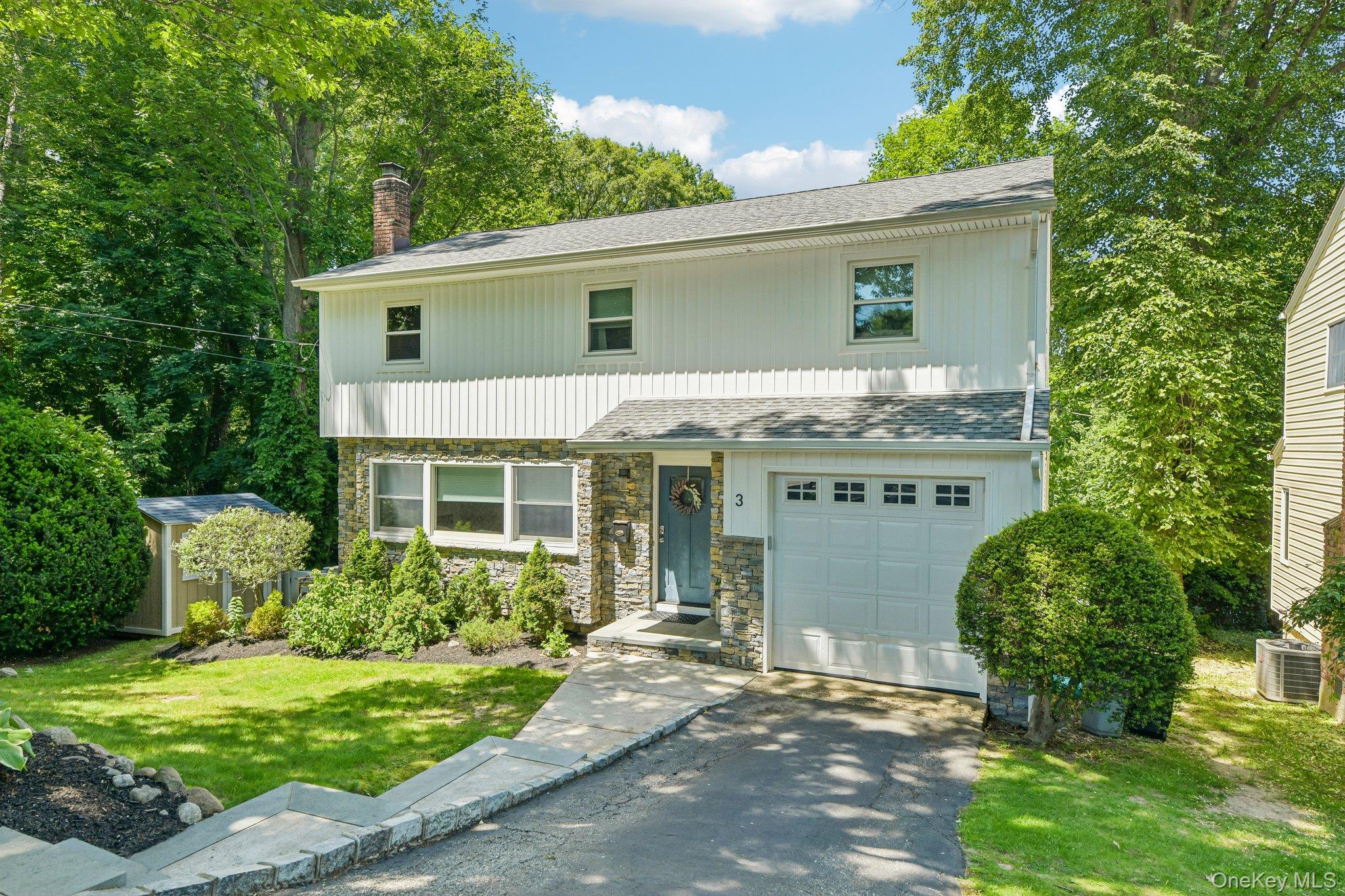 Two-story white home with stone lower facade, attached garage, and landscaped front lawn.