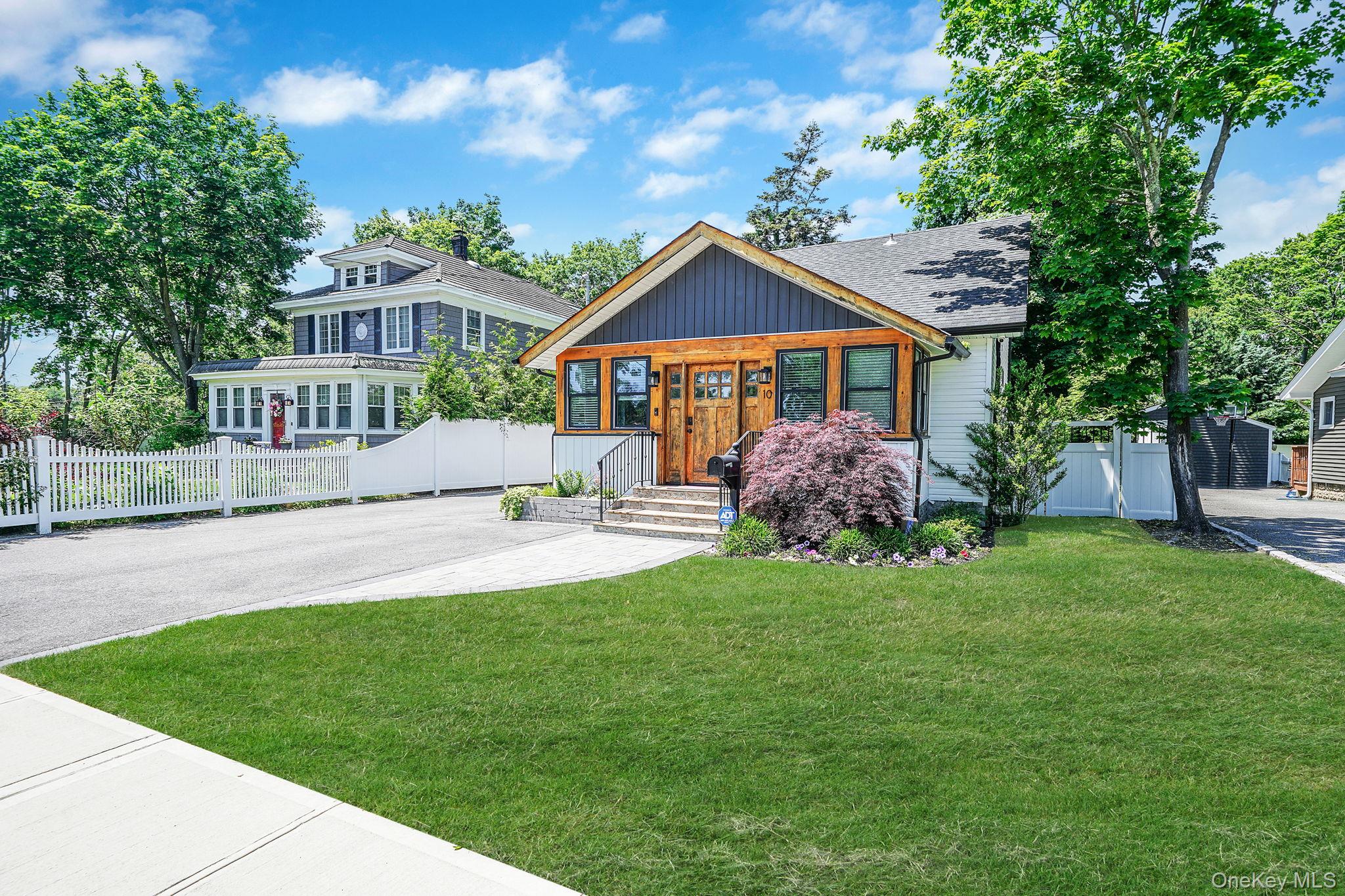 House with a wood-accented front entry, broad lawn, landscaped shrubs, and white fence.