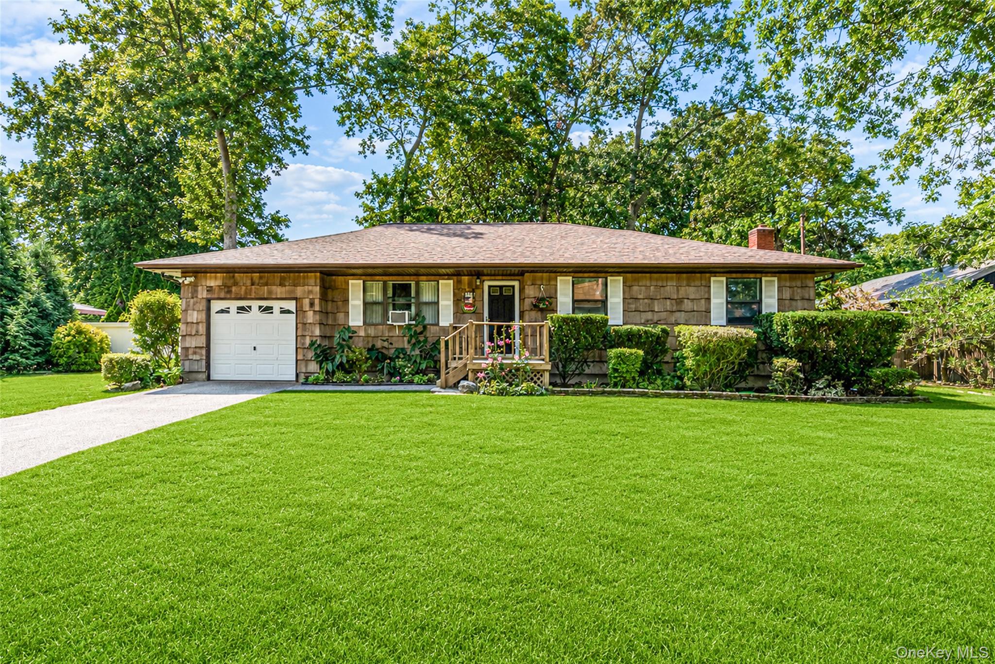 Single-story shingle-sided home with an attached garage, small porch, and broad green lawn.