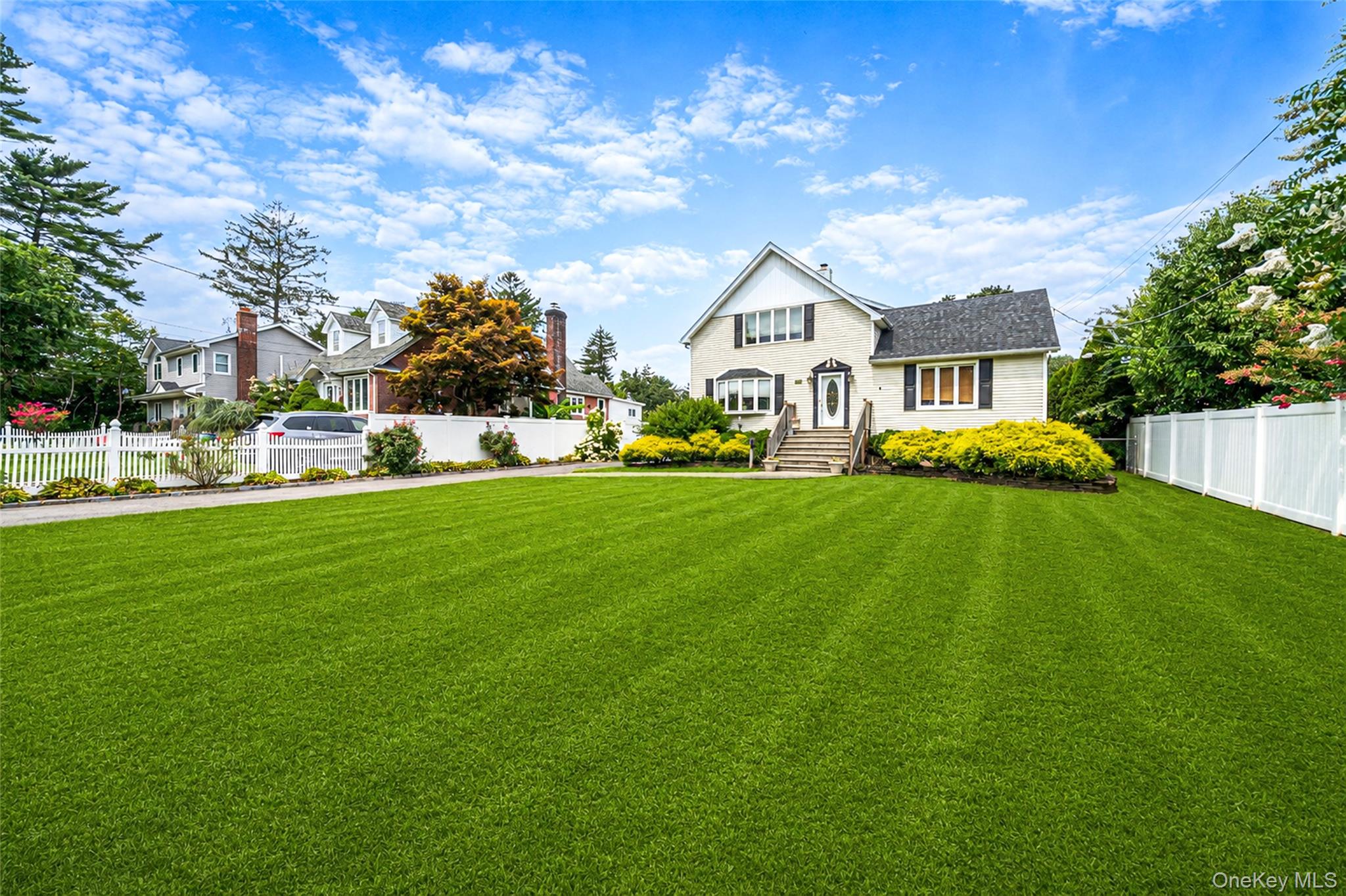 White two-story house with a front porch, fenced yard, and expansive green lawn.