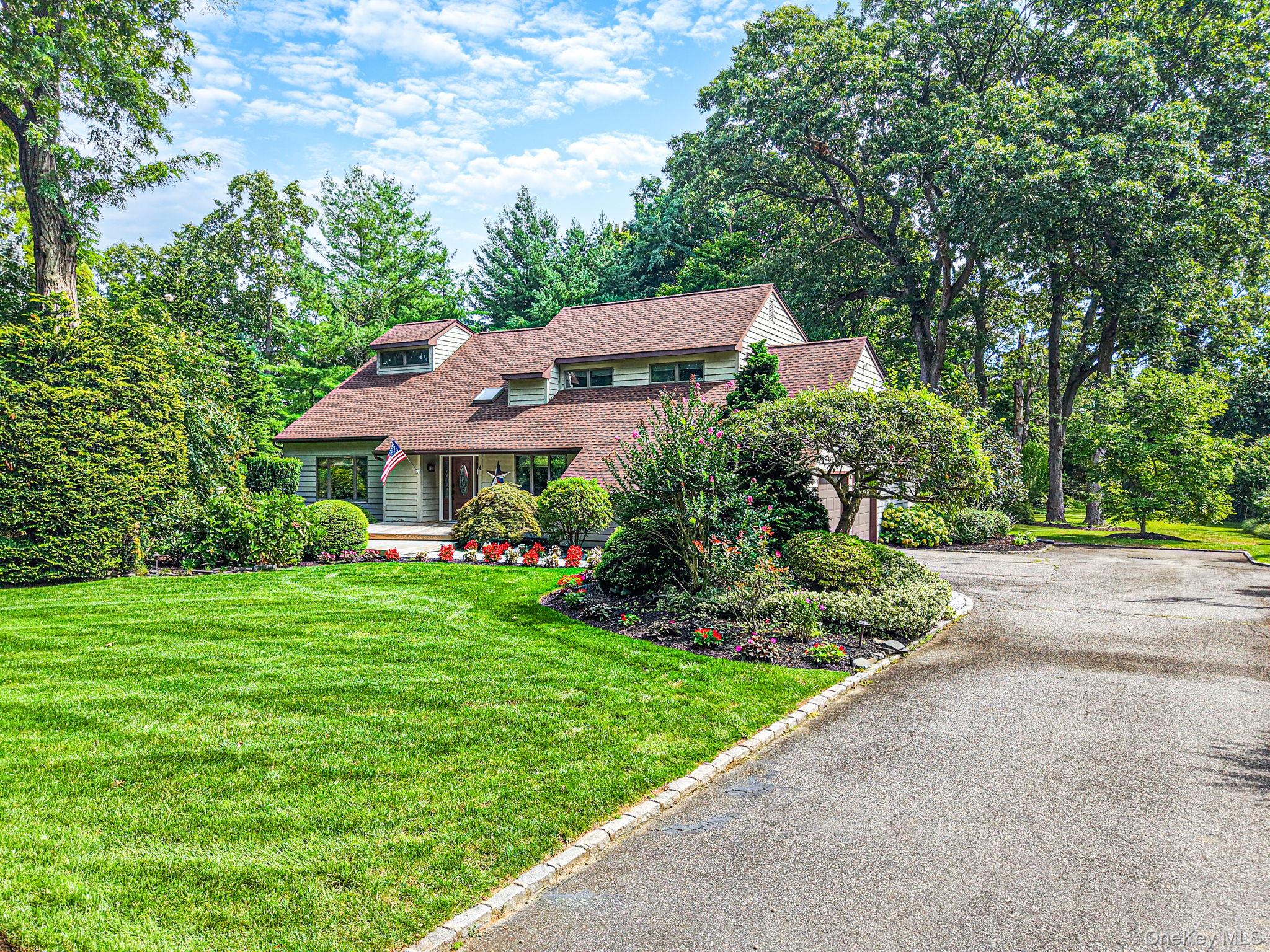 House with a broad brown roof, landscaped gardens, mature trees, and a curved driveway.