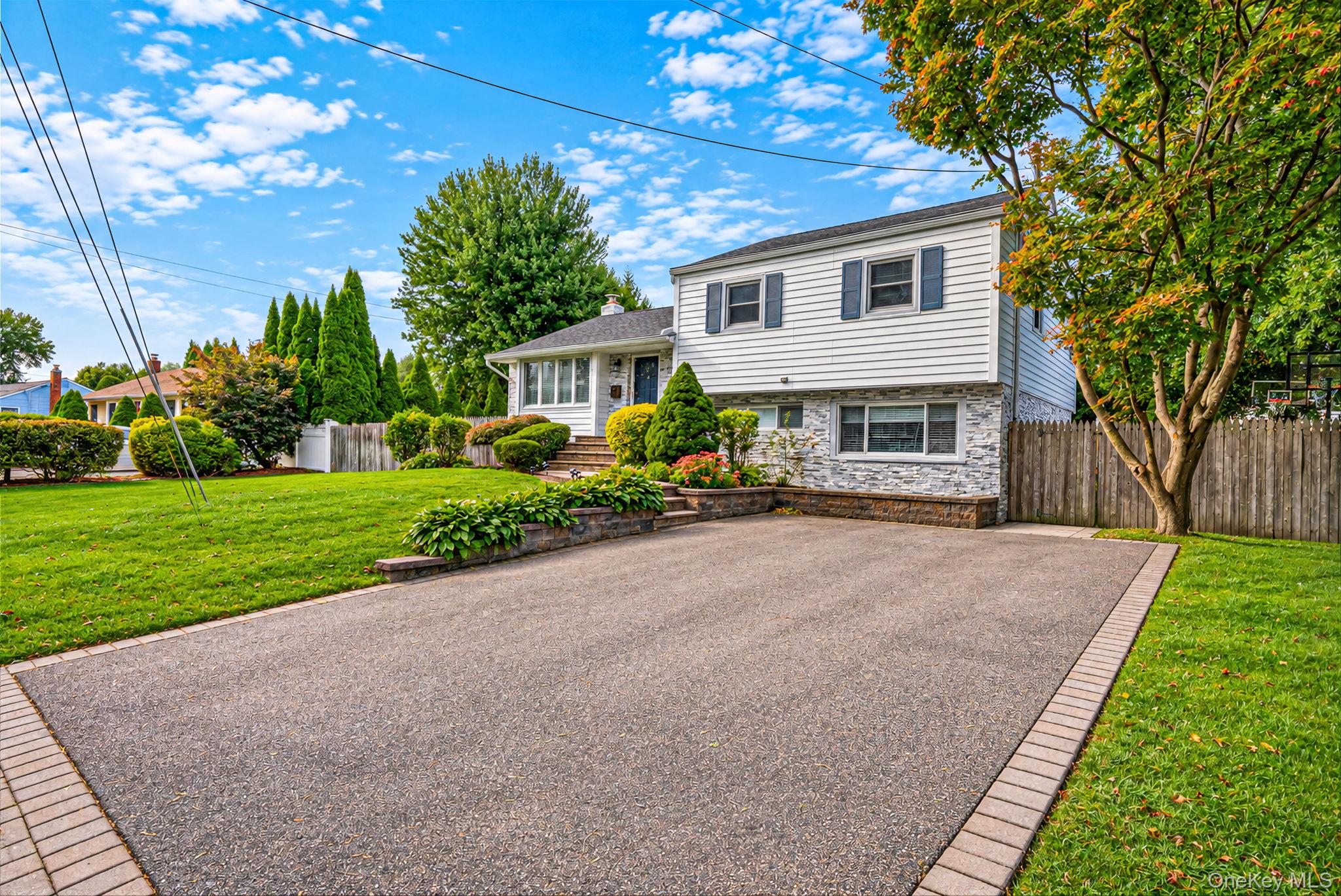 White split-level home with stone veneer, landscaped garden beds, and a broad paved driveway.
